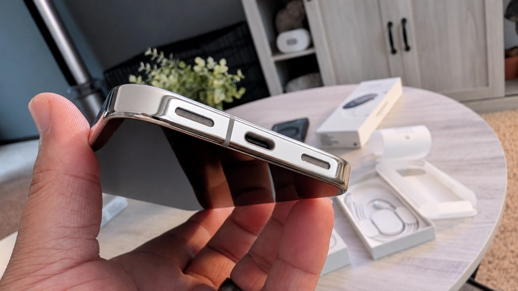 Close-up view of a hand holding a smartphone, showcasing the side with volume buttons and speaker grilles, with packaging visible in the background.