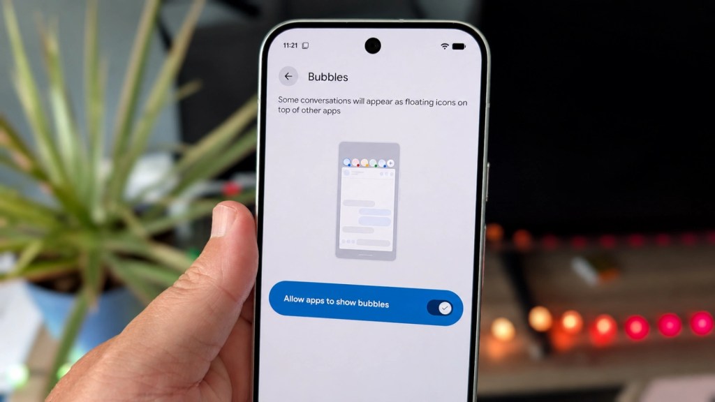 A person holding a smartphone displaying a settings page for 'Bubbles', featuring an option to allow apps to show floating icons for conversations, with a visual example on the screen.