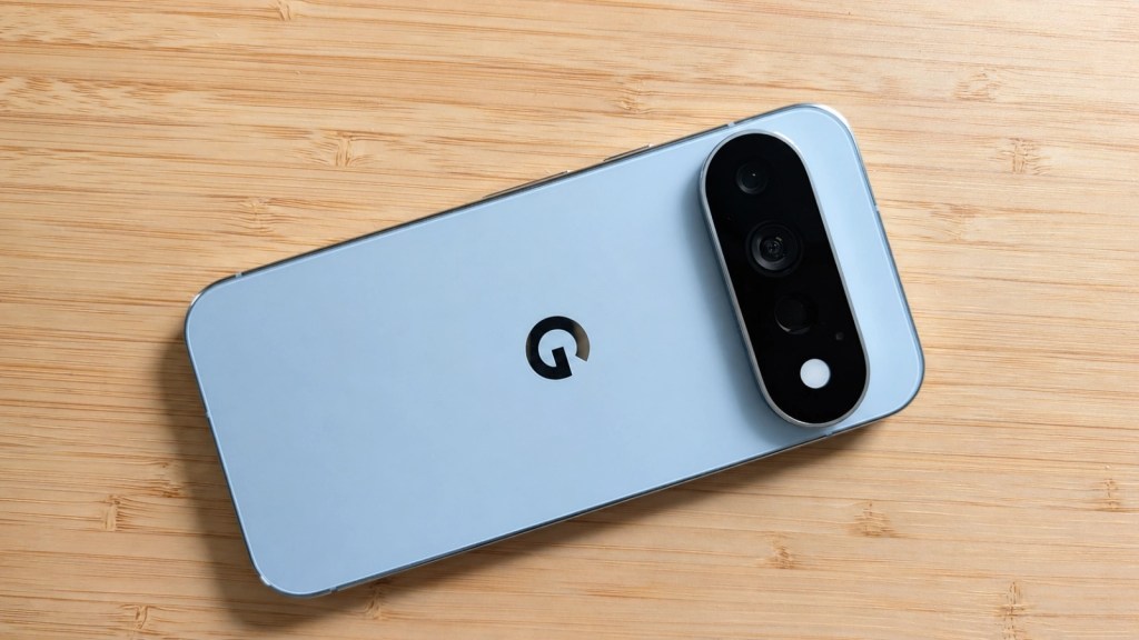 A light blue smartphone with a black camera module, featuring three lenses and the letter 'G' logo on the back, placed on a wooden surface.