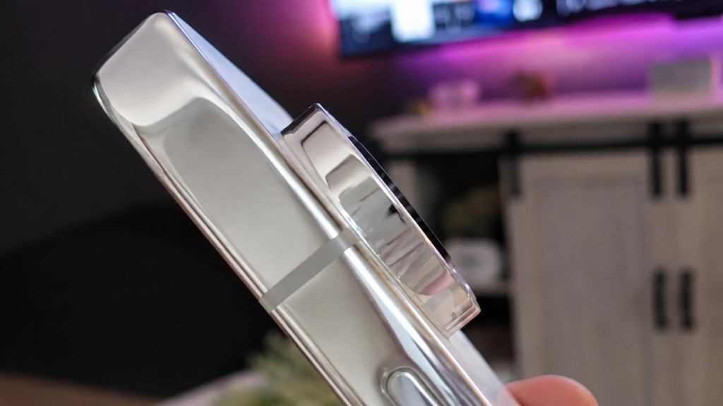 Close-up of a sleek silver device with a round camera lens, held at an angle against a blurred background.