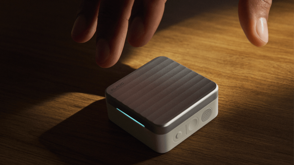 A close-up of a small, modern device with a textured surface, placed on a wooden table, as a hand hovers above it.