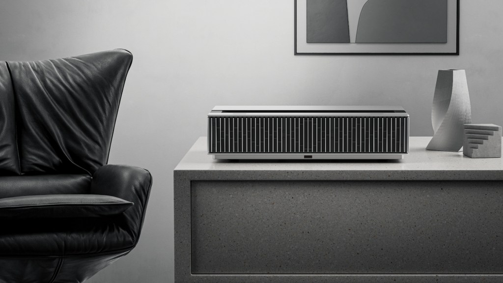 A modern audio device on a stone tabletop next to decorative objects and a black leather chair.