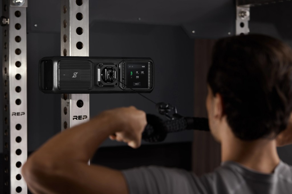 A person performing an exercise using a high-tech fitness device mounted on a wall, displaying workout metrics.