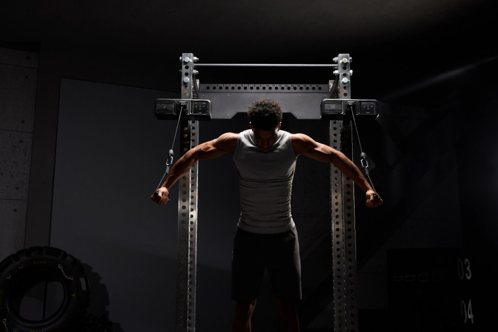 A man performing a cable fly exercise in a dimly lit gym, showcasing strong upper body muscles.