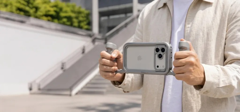 A person holding a smartphone in a protective case with handles, standing in an outdoor setting with a modern building in the background.