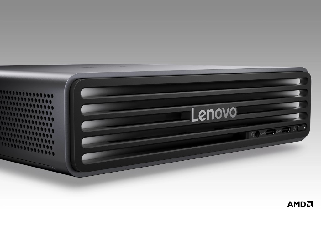 A close-up view of a Lenovo desktop computer with a sleek design, featuring ventilation grills and various ports on the side. The front displays the Lenovo logo prominently.