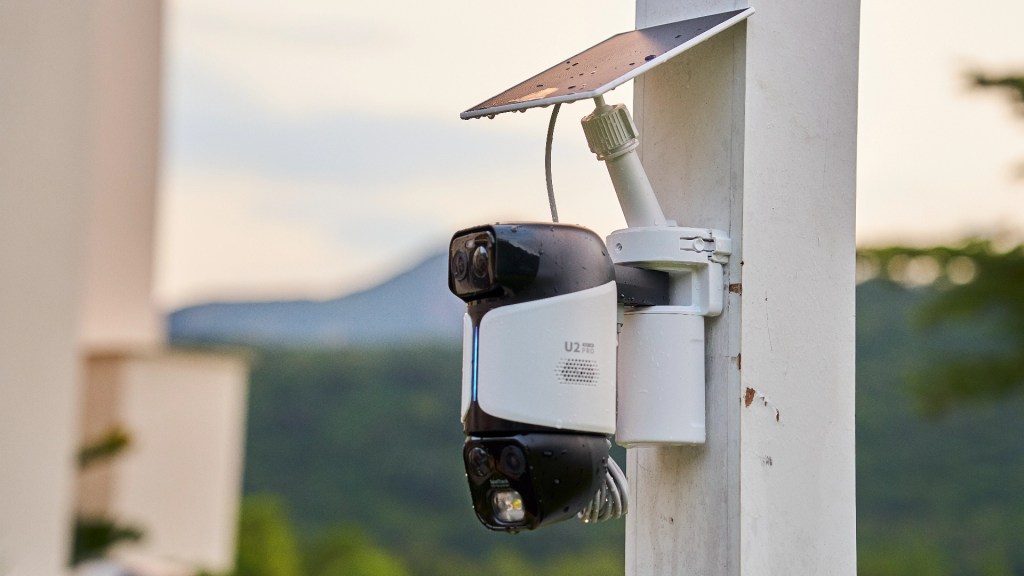 A security camera mounted on a pole with a solar panel, surrounded by a natural landscape.