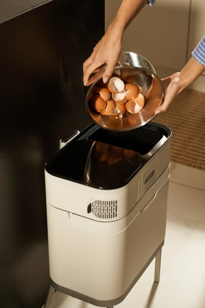 A person pouring eggshells from a bowl into a modern trash bin in a kitchen setting.
