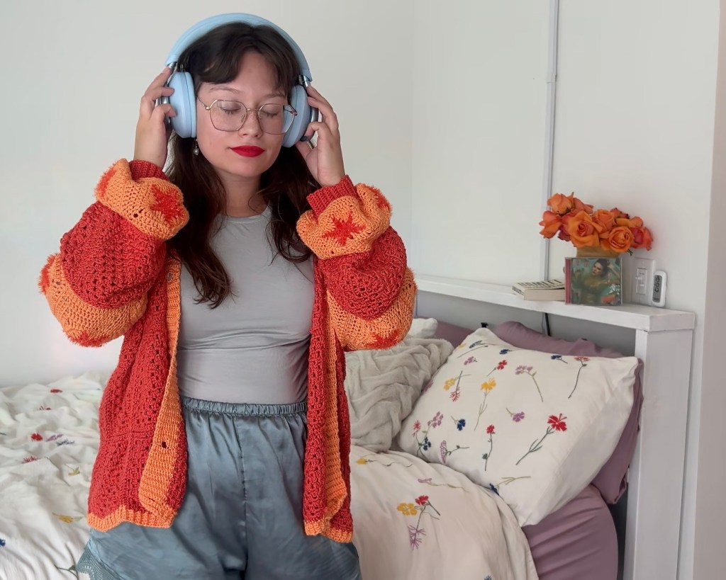 woman in headphones with bright orange crochet cardigan standing