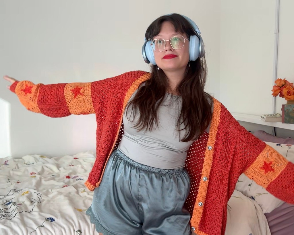 woman in blue headphones in bright orange crochet cardigan with stars 