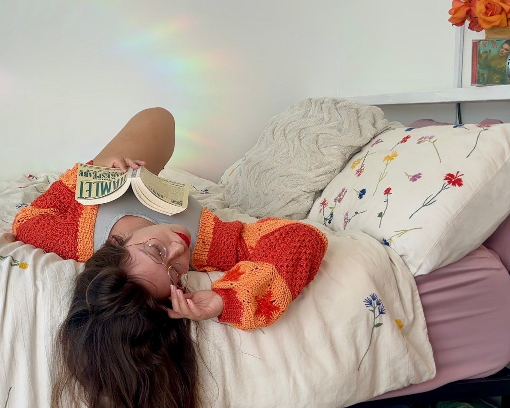 woman lying on bed with hamlet in bright orange crochet cardigan