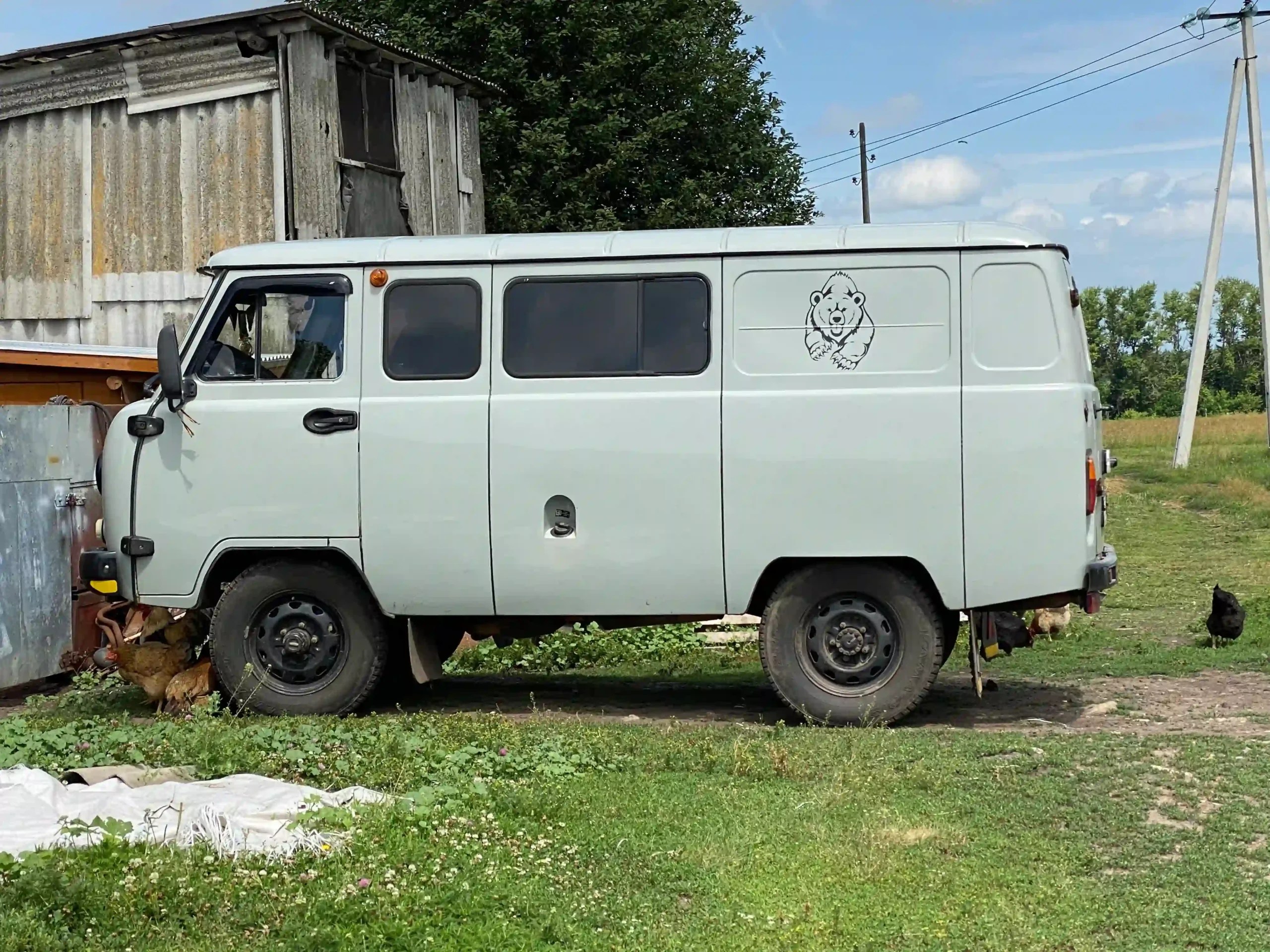 White UAZ van with a cartoon bear parked beside a rural home