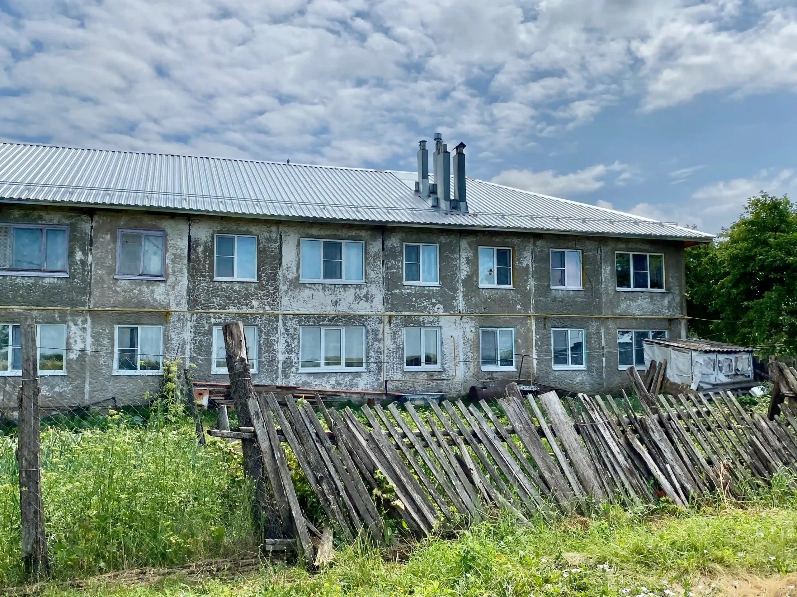 Weathered two-story residential building behind an old wooden fence