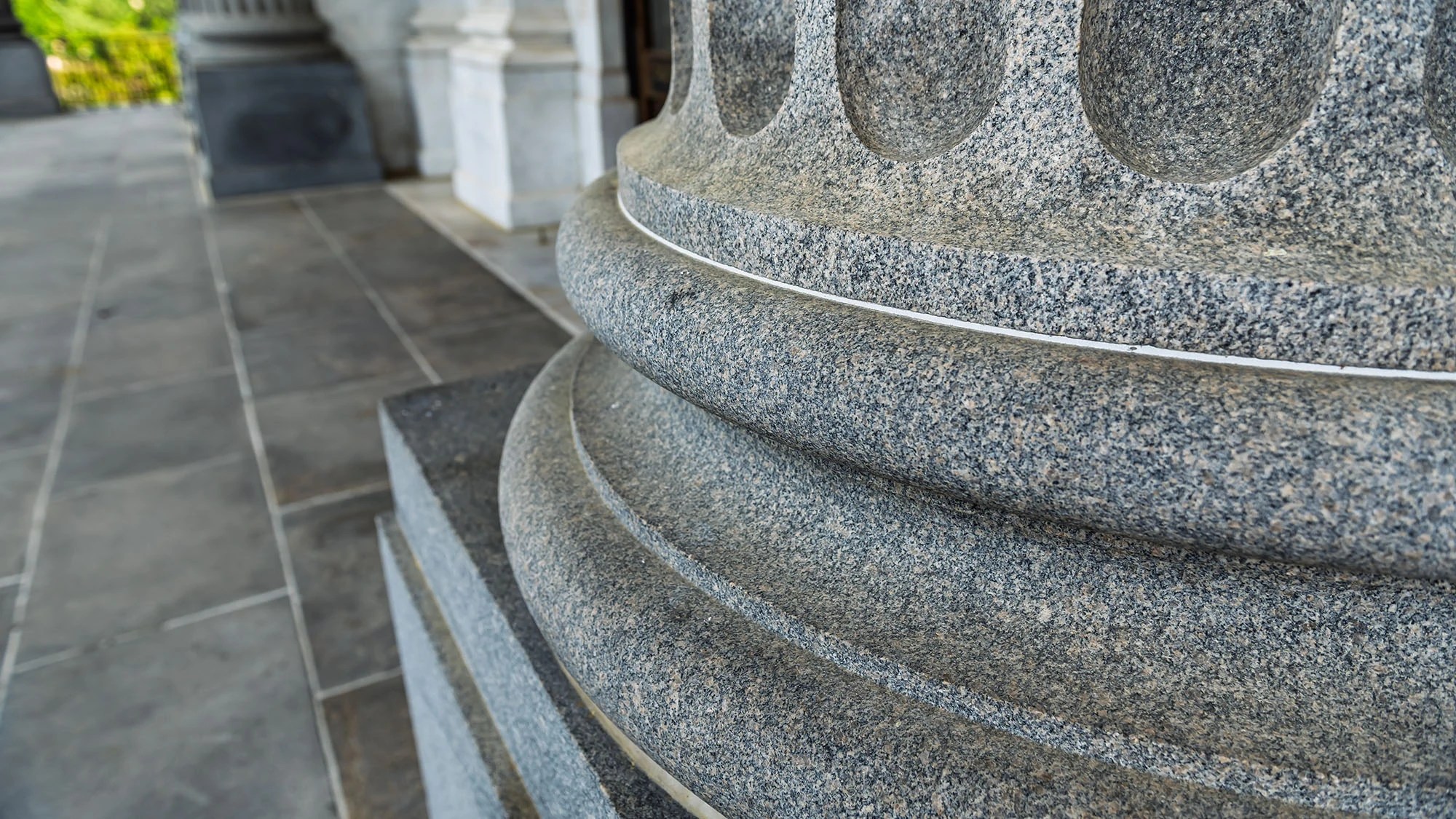 Close-up detail of a granite column base at the South Carolina State Capitol in Columbia, showing stacked torus moldings and the fine texture of gray speckled granite against a stone tile floor.