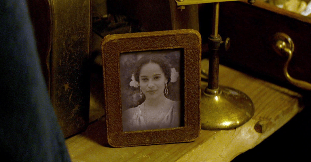 Captura do filme Animais Fantásticos e Onde Habitam. Nela, vemos a personagem Leta Lestrange num porta retrato em meio a outros itens de Newt Scamander. Na foto, Leta está jovem, usa adereços brancos no cabelo, está de vestido branco e sorri.