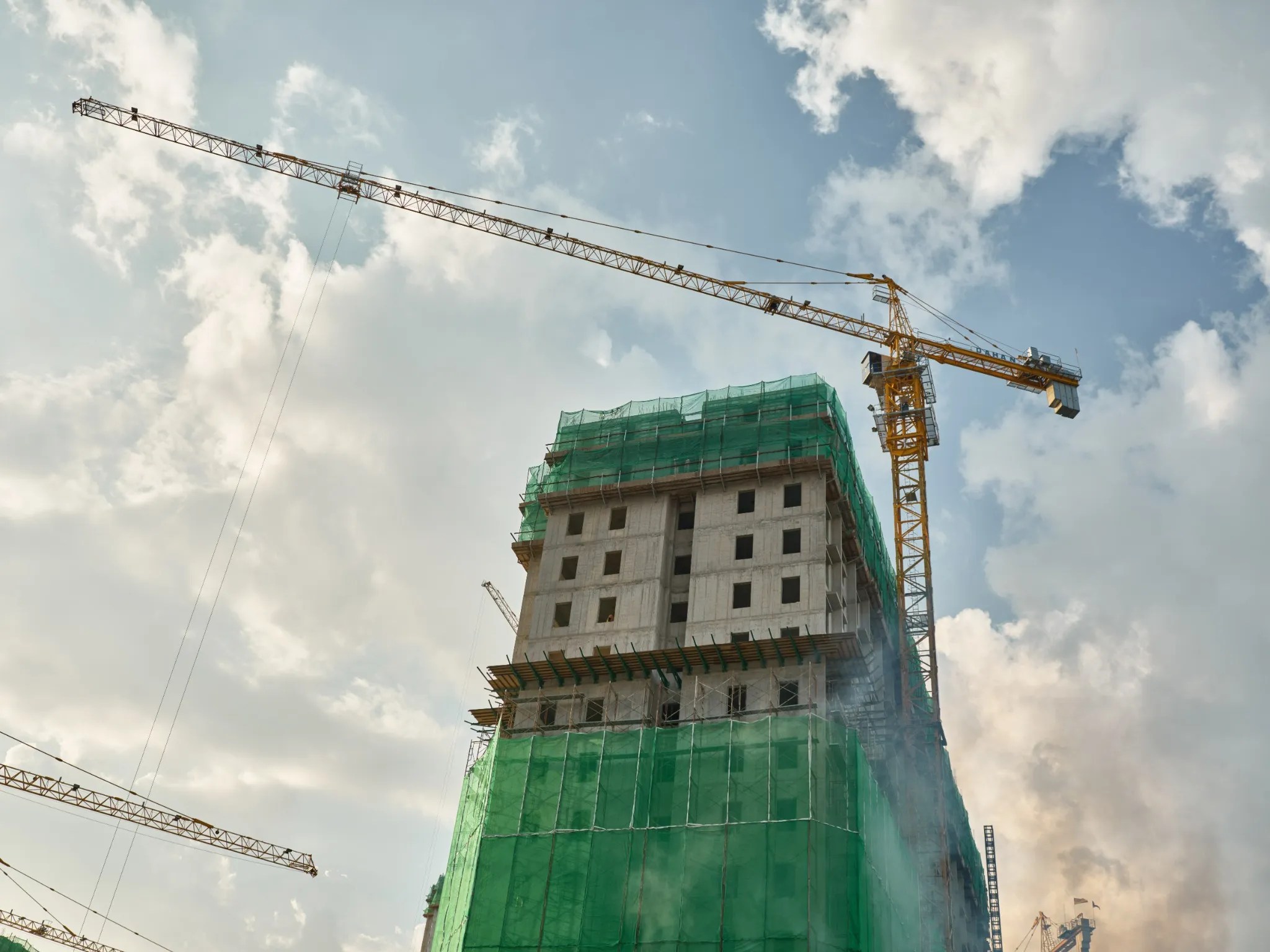Foto de un edificio en construcción con andamios y una grúa amarilla detrás.