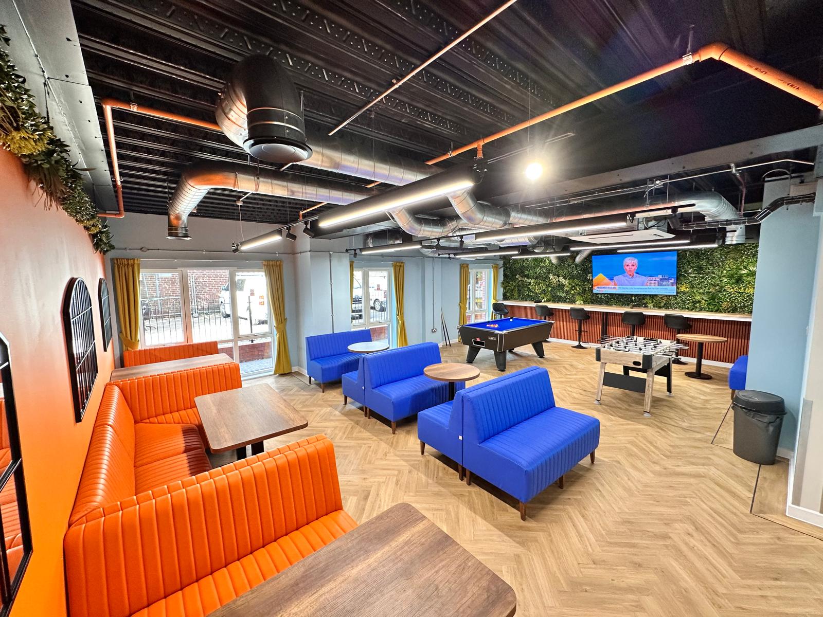 Lounge with orange and blue chairs and a pool table.