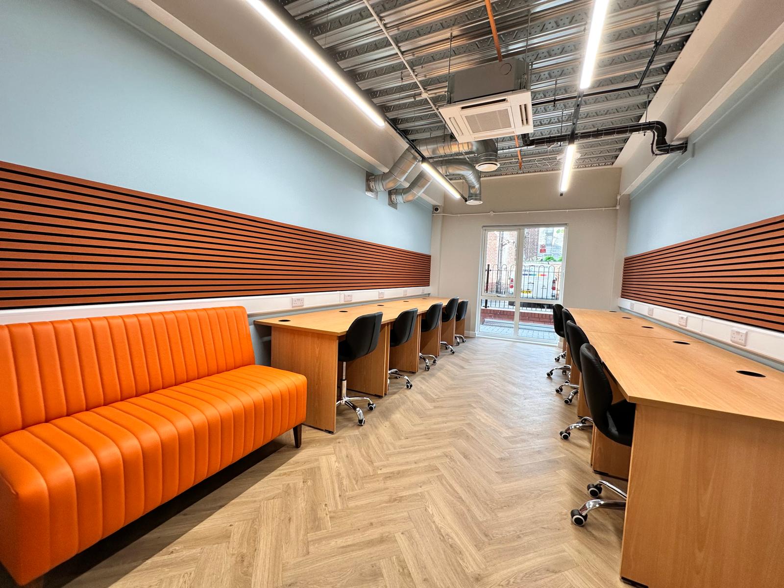 An orange sofa with a long row of desks and multiple chairs.