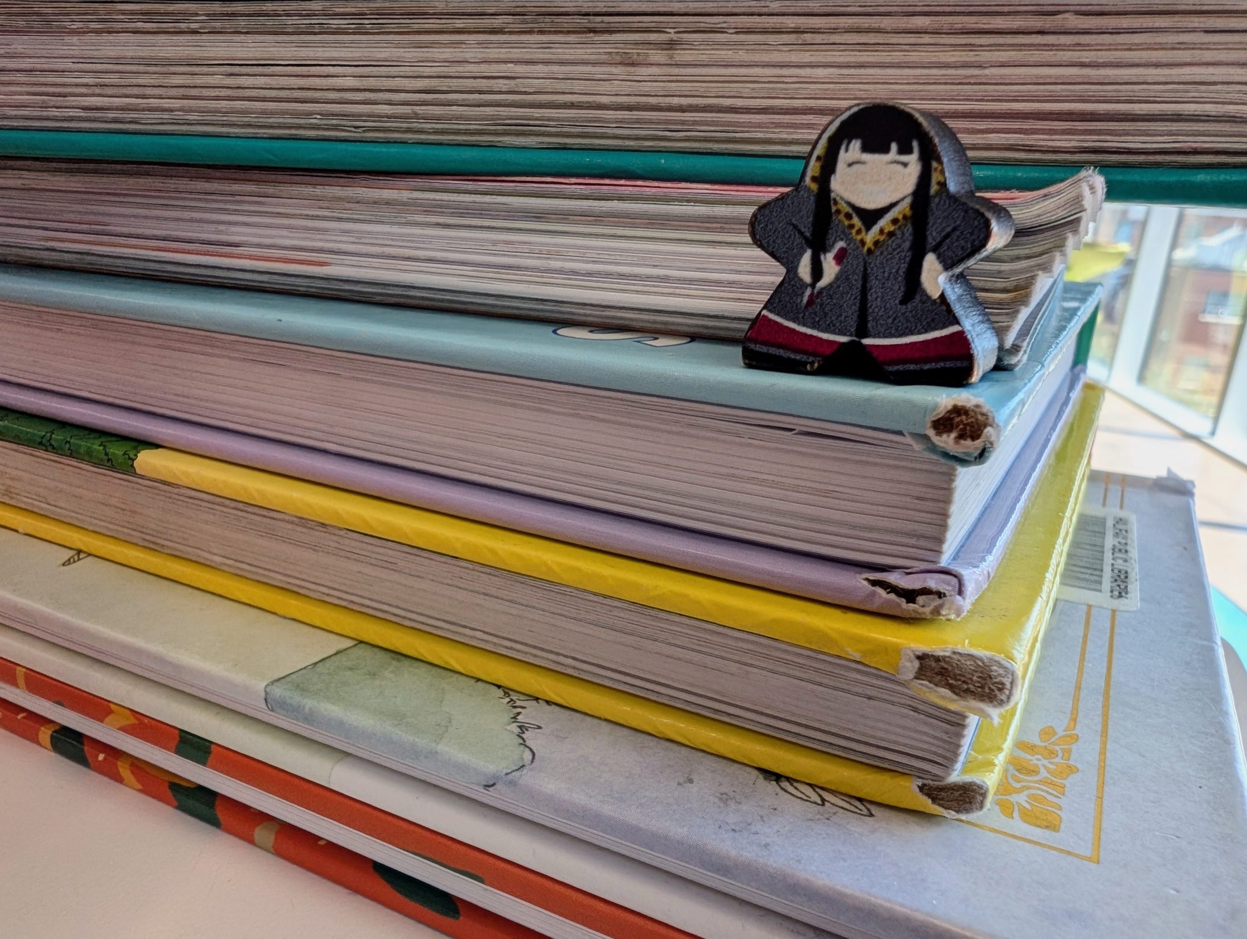 A meeple of a woman holding a paintbrush stands on a stack of hardcover books.