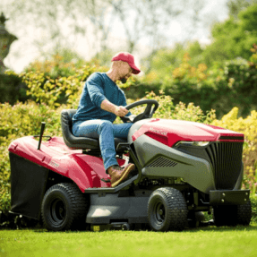 Man operating a Mountfield lawn mower in a garden setting.