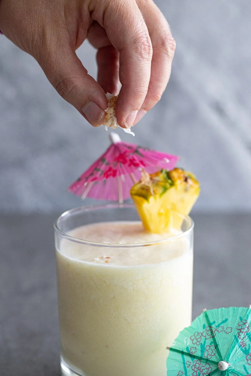 Woman sprinkling toasted coconut on top of a pina colada.