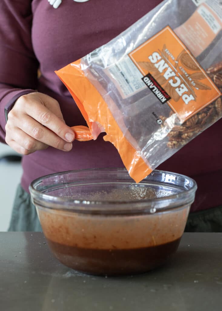 Woman pouring pecans into pie mix.