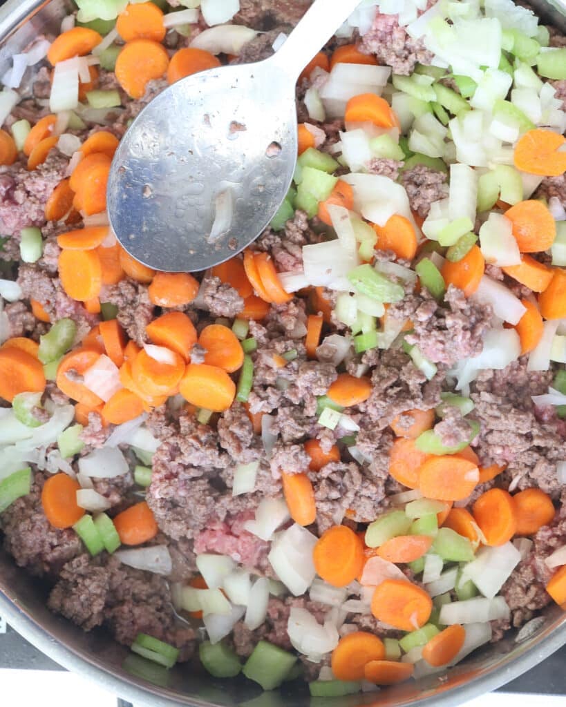 Ground beef with carrots and celery in a stainless steel pan.