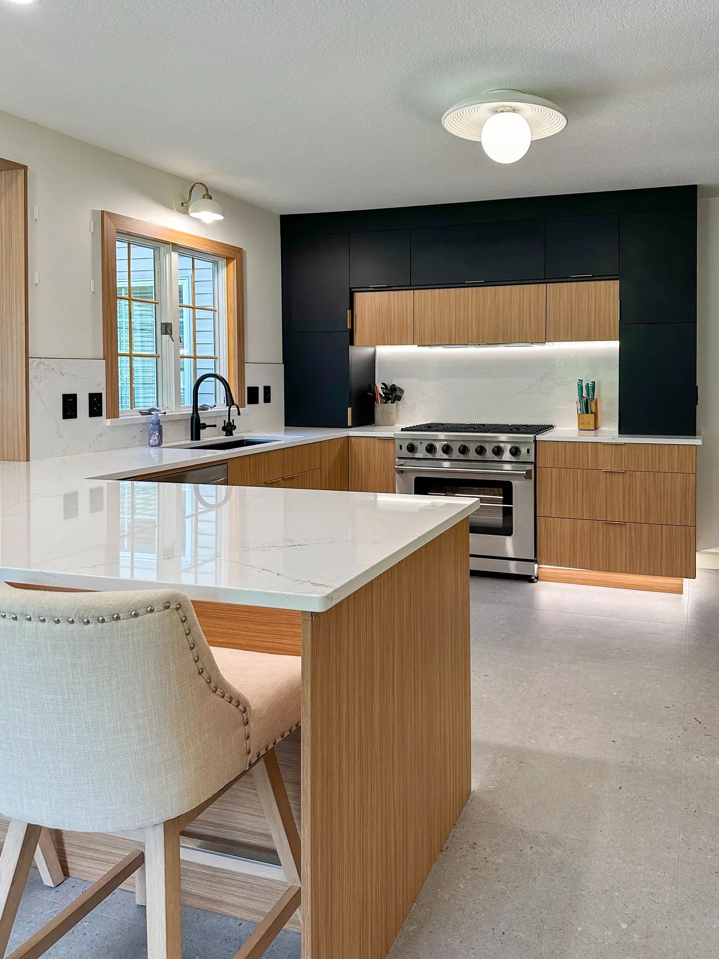 Black Maple Mid-Century Kitchen with satin black and maple wood grain acrylic-wrapped European slab cabinets, quartz countertops, full-height quartz backsplash, hidden vent hood, under-cabinet lighting, island seating, black fixtures, and gray cobblestone flooring.