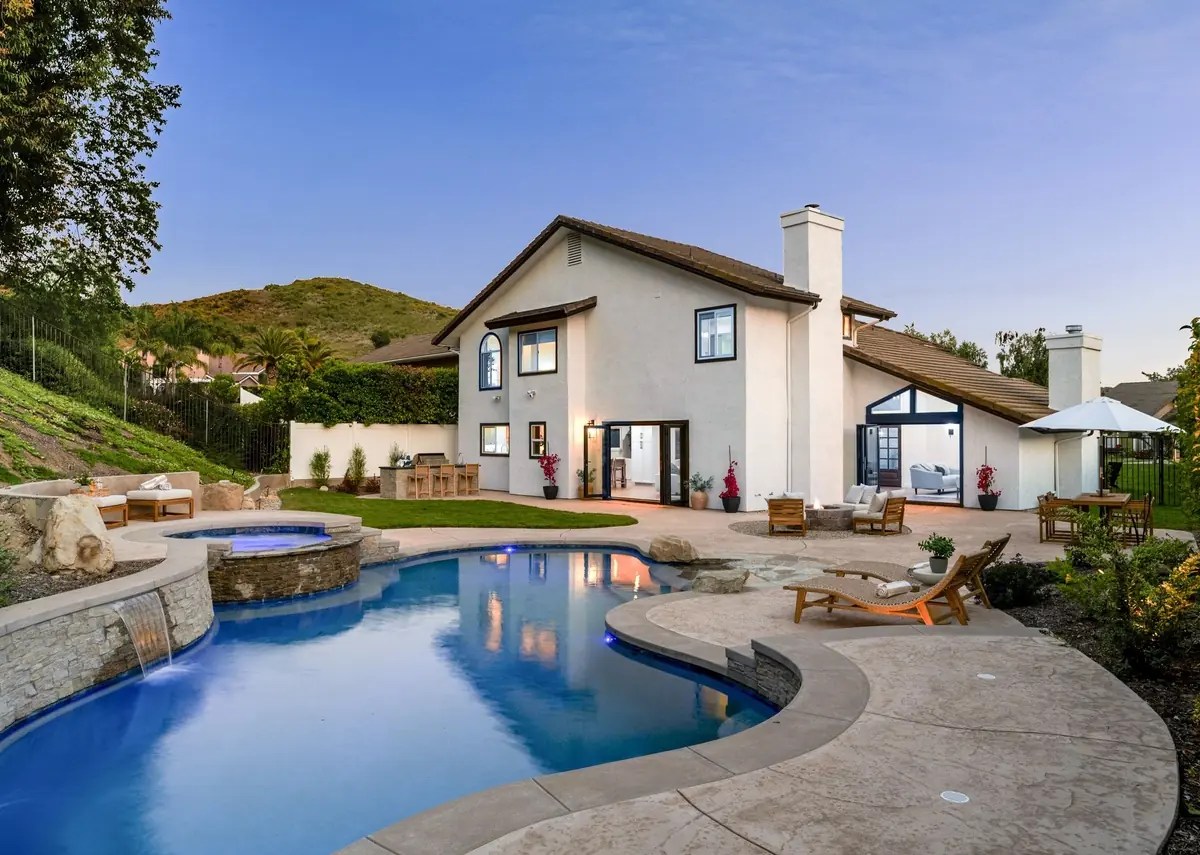A large backyard space with a freeform swimming pool and integrated spa installed next to a grass-covered hill.