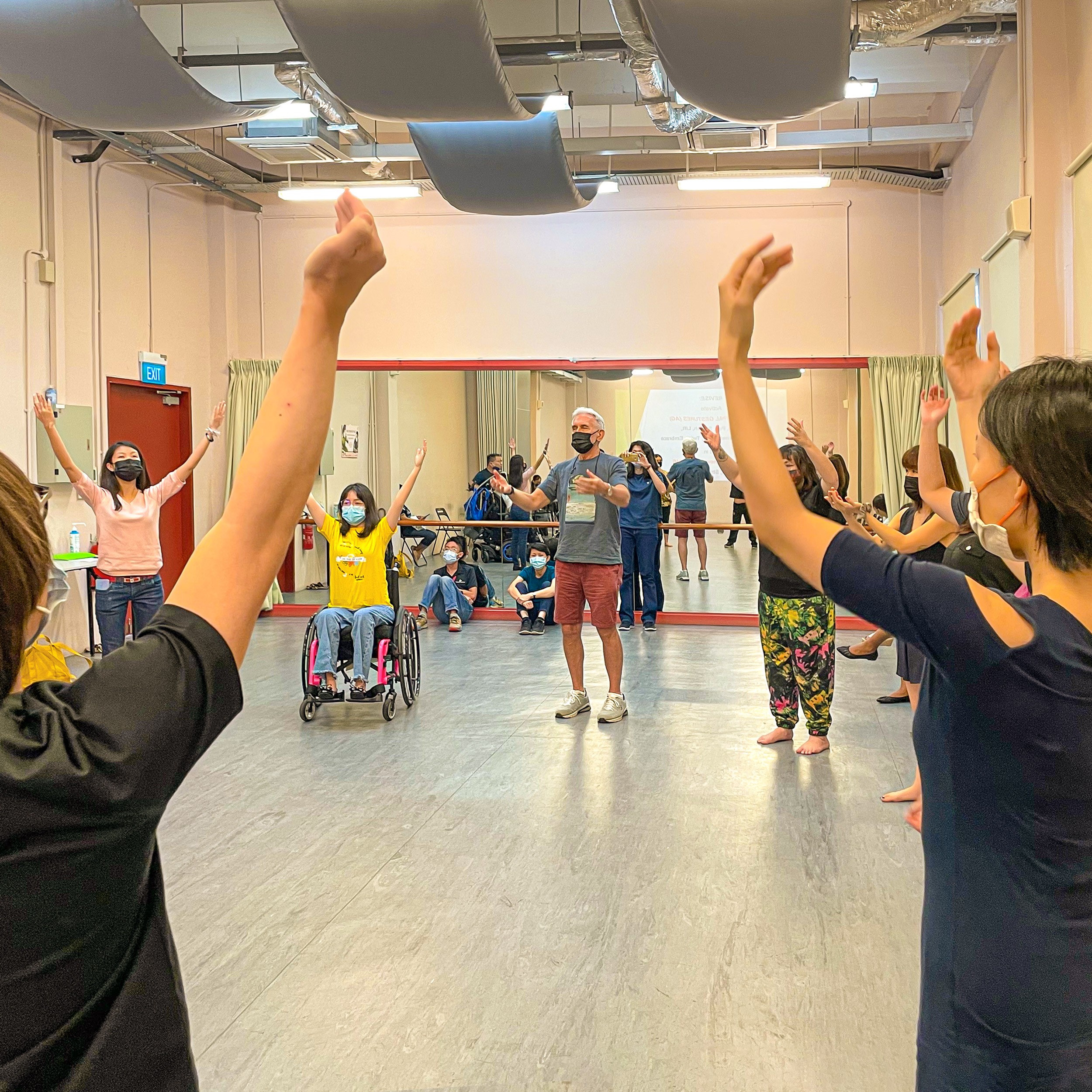 This image features participants standing in a circle, with both arms raised above their heads as they inhale and exhale.