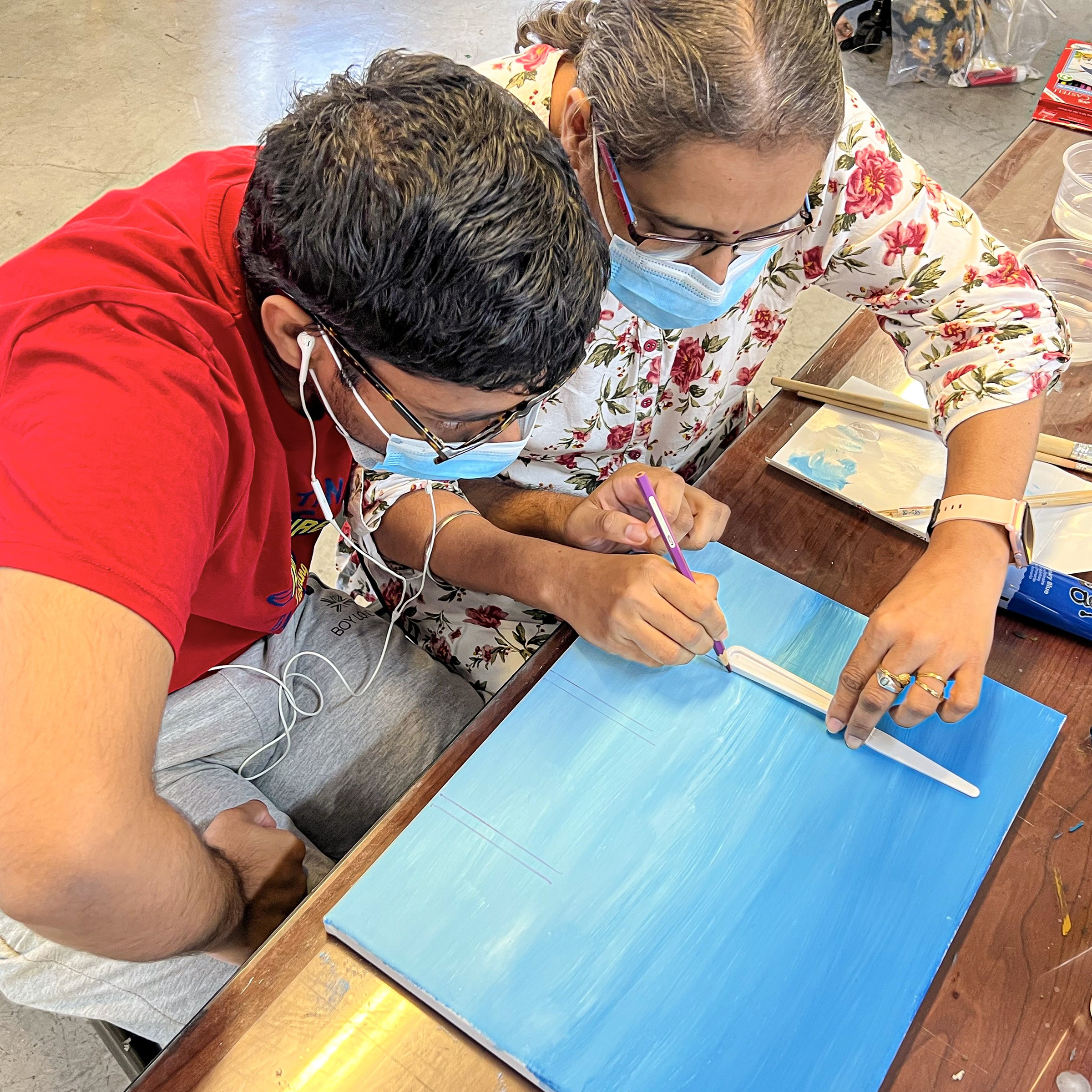 This image features an autistic participant working with his mother to create a painting that employs everyday objects as stencils.