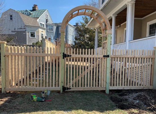 Wooden picket fence and arbor with gate leading into a backyard designed and installed by Artistic Fence company