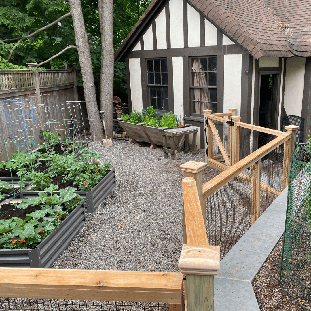 Wood and wire garden fencing around a vegetable garden with a tudor style home in the background