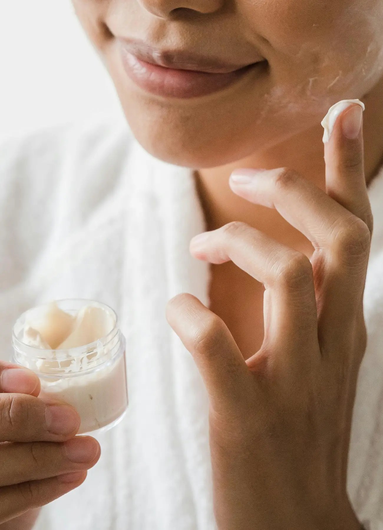 A person applying face beauty cream to their face.