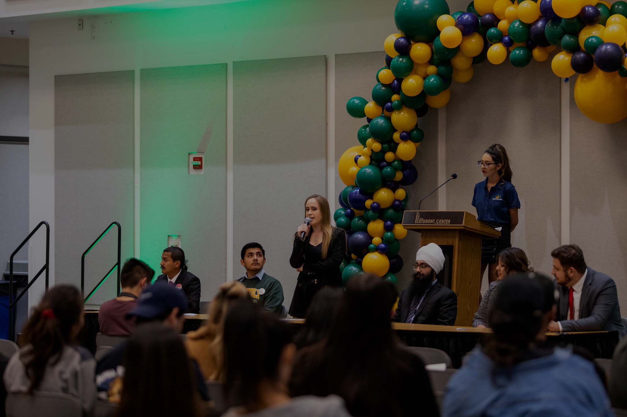 person talking in front of a podium to an audience