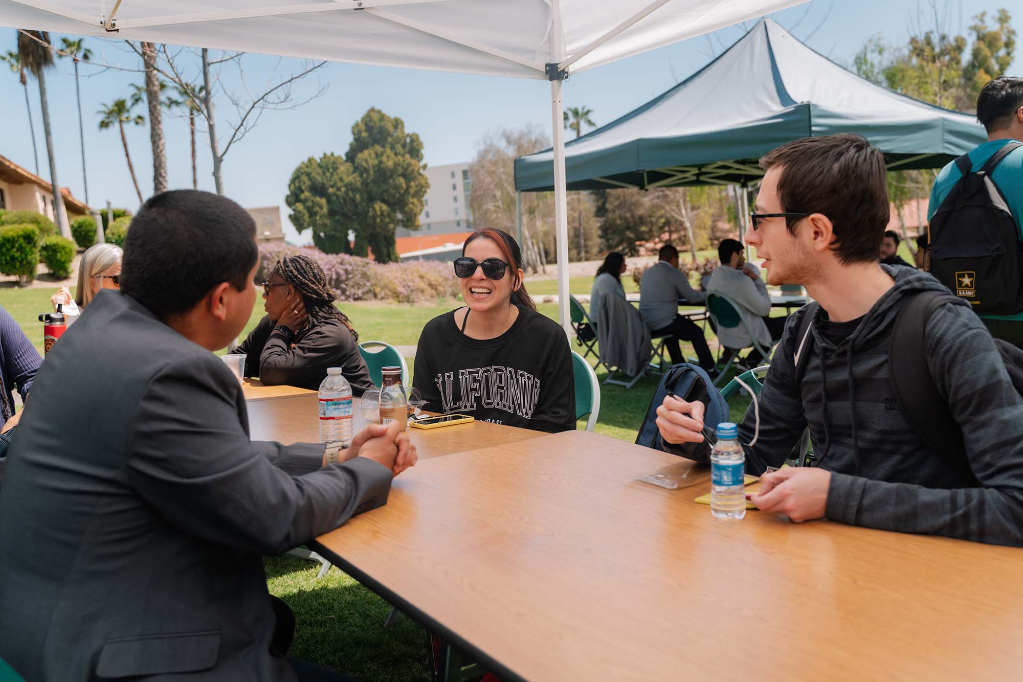 individuals talking while sitting at a table outside under a canopy