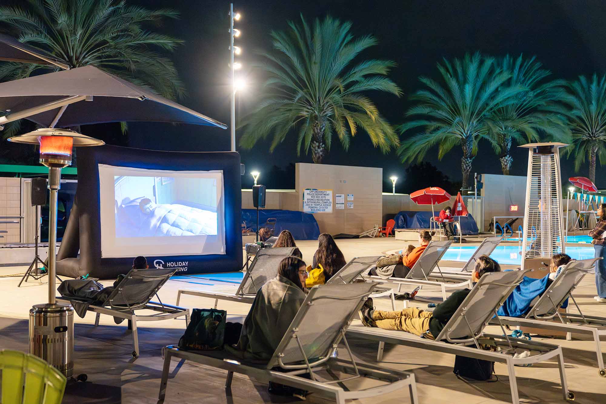 participants sitting on lawn chairs watching an outdoor movie by the pool