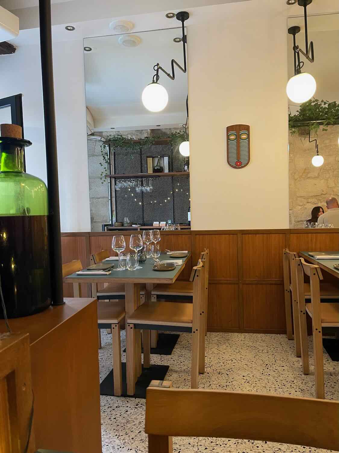 A view inside H&eacute;b&eacute; restaurant in Paris, characterized by its modern yet welcoming design. The dining area is calm with natural wood furniture, terrazzo flooring, and stylish globe lighting, ready to host diners in a casual, chic setting.