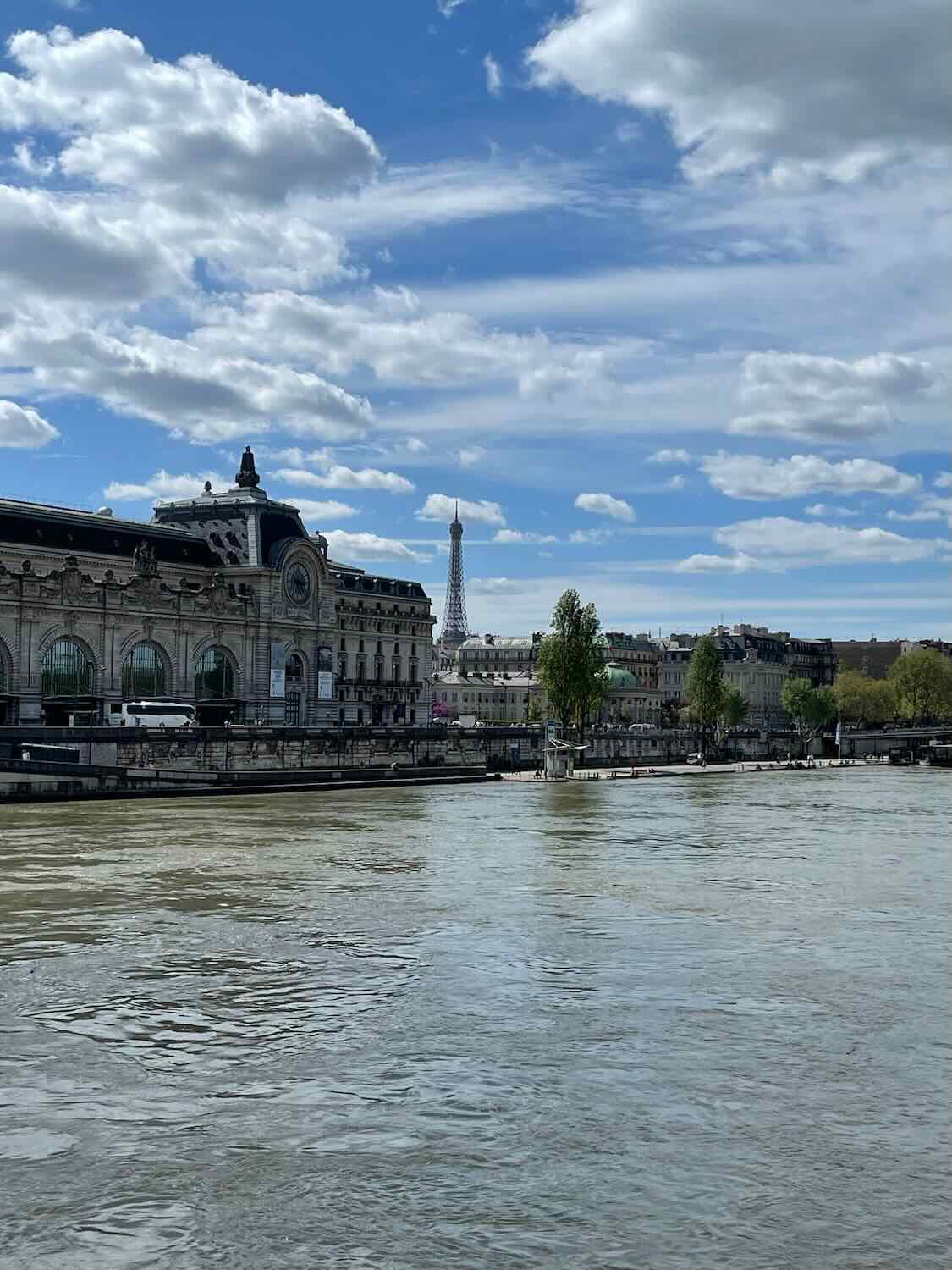 A clear day view of the Seine River with the Mus&eacute;e d'Orsay on one bank and the Eiffel Tower in the far background, showcasing Paris's iconic architecture and waterways.