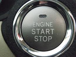 Close-up of an "Engine Start Stop" button in a vehicle, perfect for renting a car. The button is encased in a sleek metallic ring.