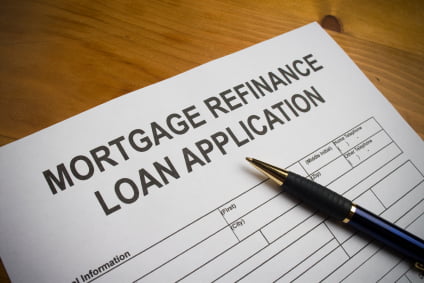 A pen rests on top of a refinance loan application form placed on a wooden surface.