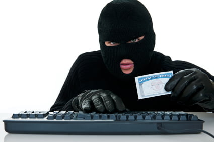 A masked person in black gloves holds an ID card while using a keyboard, suggesting identity theft or the creation of a new social security number for cybercrime purposes.