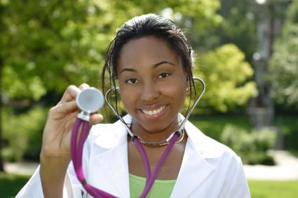 A woman in a white coat holds a stethoscope towards the camera, with a background of greenery, embodying the dedication and hands-on experience of a work study program.