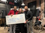 Three people, beaming with joy, proudly hold a large check in a brick-walled room filled with audio equipment—a promising step towards their budget goals.
