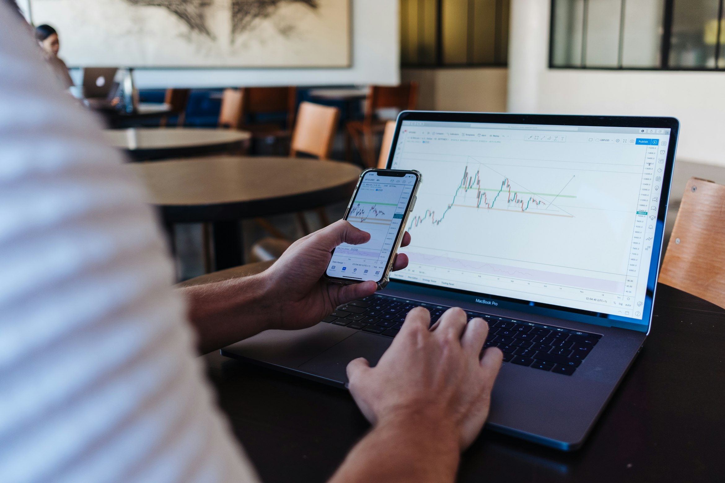 In a modern office setting, a person uses a smartphone and laptop to analyze financial graphs, seeking important tips for stock investment.