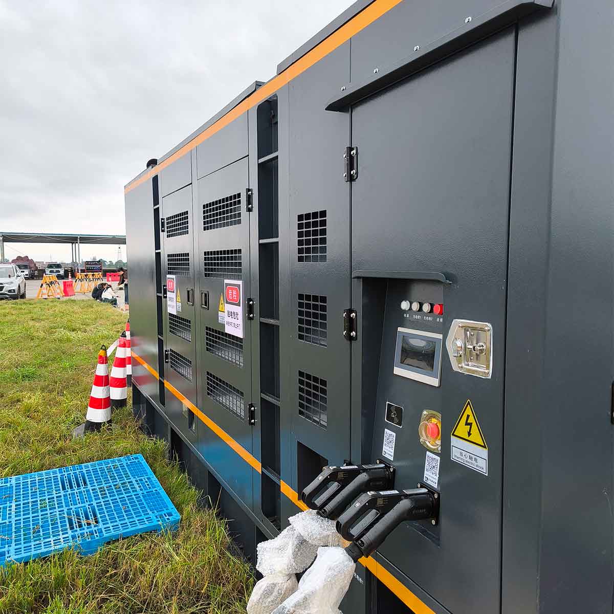 A large industrial methanol generator set in a grey enclosure with yellow stripes, featuring a control panel and charging cables on an outdoor grassy field