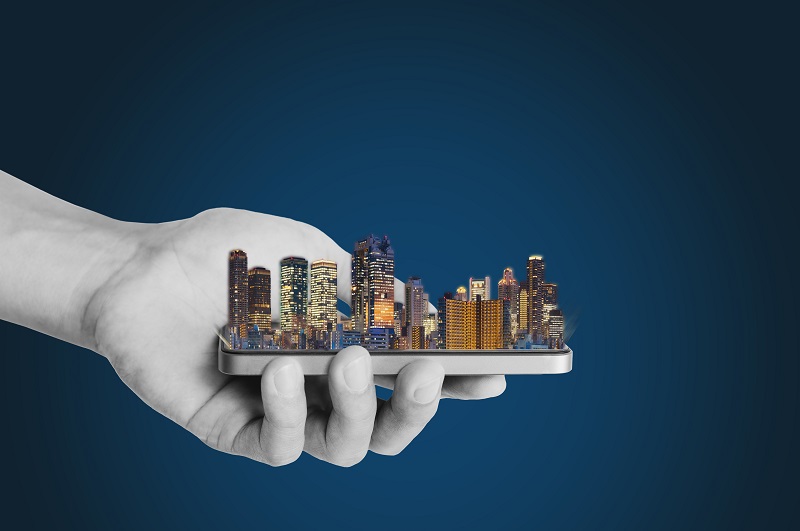 Smart city, smart building, and real estate business. Businessman hand holding mobile smart phone with modern building on blue background