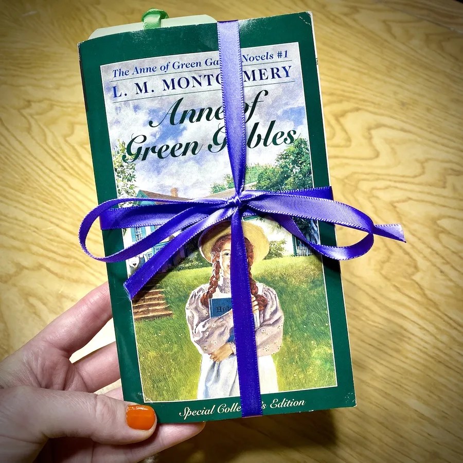 Purple ribbon tied in a bow around a book to secure the bookmark inside.