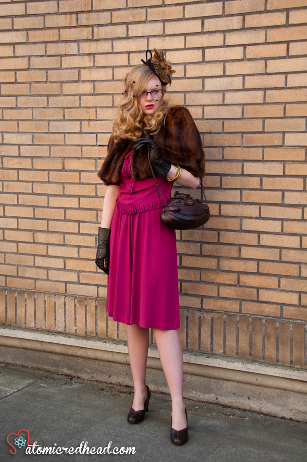 An all vintage ensemble. A hat made to look like it has two birds perched atop, a mink caplet, magenta 40s dress, a purse made out of an armadillo, vintage leather gloves, and alligator shoes.
