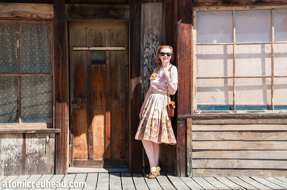 Standing in my outfit I themed for the day, a vintage pale pink nylon blouse, with a vintage border print skirt featuring an illustration of a western town.